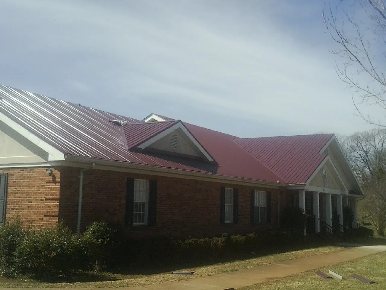 Red metal roof with gabled entries on a long brick building, from a Hail Damage Roof Repair job in Elliott