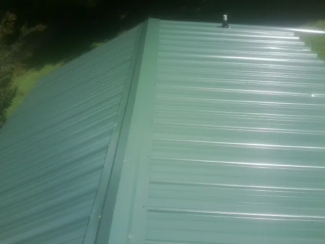 New green metal panels meeting at the ridge of a roof — Flat Roof Repair work by our crew in Elliott