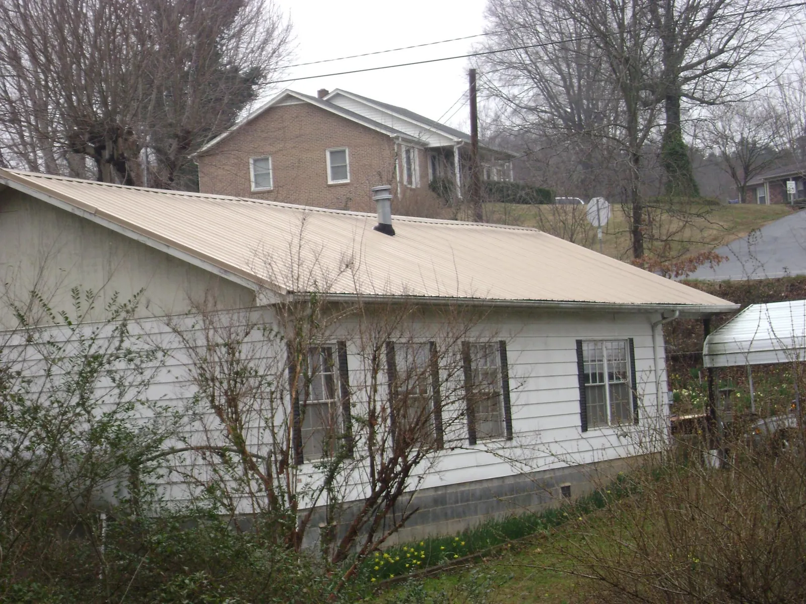 Tan metal roof on a white sided house set into a hillside — Commercial Roofing by Roofing Brothers in Elliott